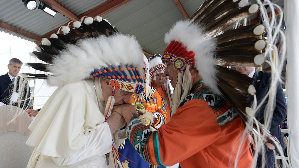 El papa Francisco besa la mano de un representante indígena canadiense.