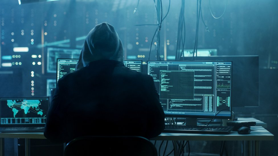 Hacker delante de varias computadoras.