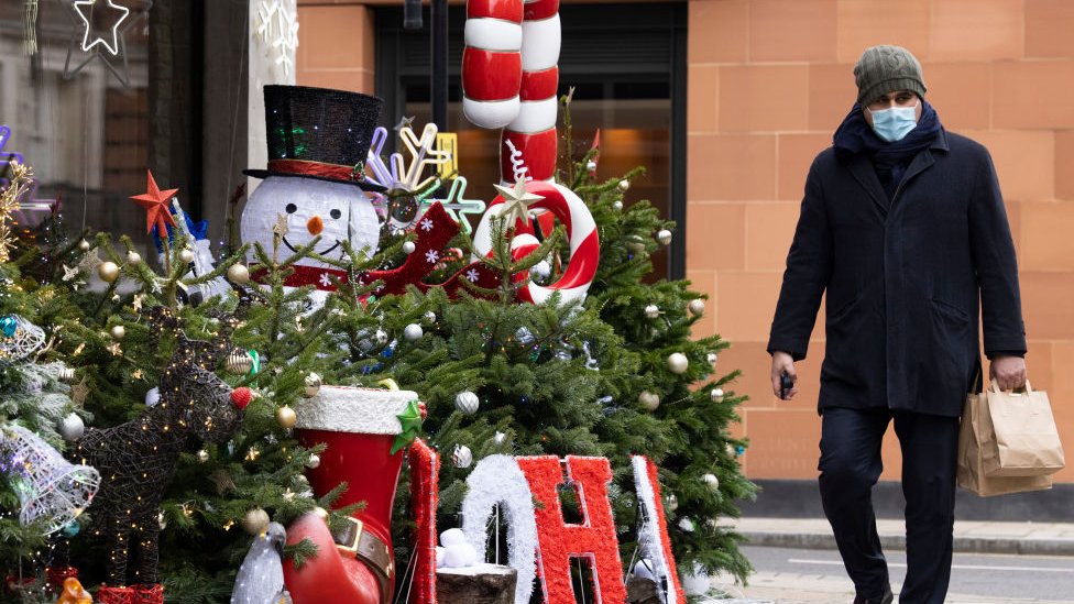 A man wearing a facemask walks past Christmas decorations outside a wine shop in Mayfair, central London