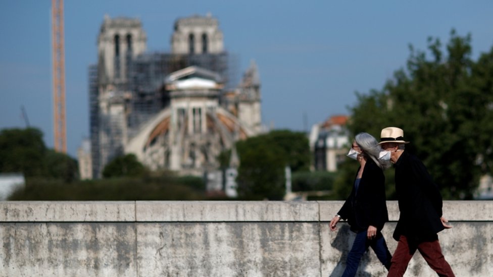 Два человека в масках проходят мимо Нотр-Дам в Париже