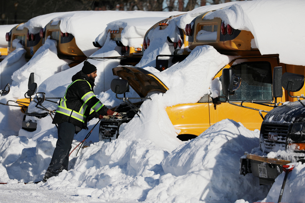رجل يحاول تشغيل محرك حافلة مدرسية غمرتها الثلوج، بعد تساقط ثلوج كثيفة في سكاربورو، أونتاريو، كندا.