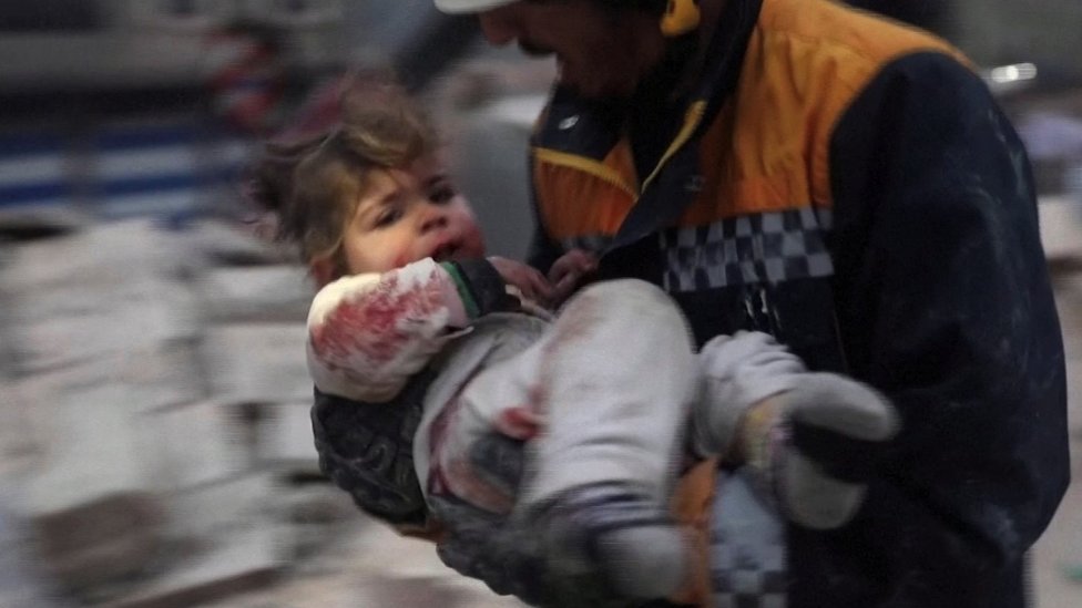 A rescuer carries a Syrian toddler, Raghad Ismail, away from the rubble of a building following an earthquake in rebel-held Azaz, Syria