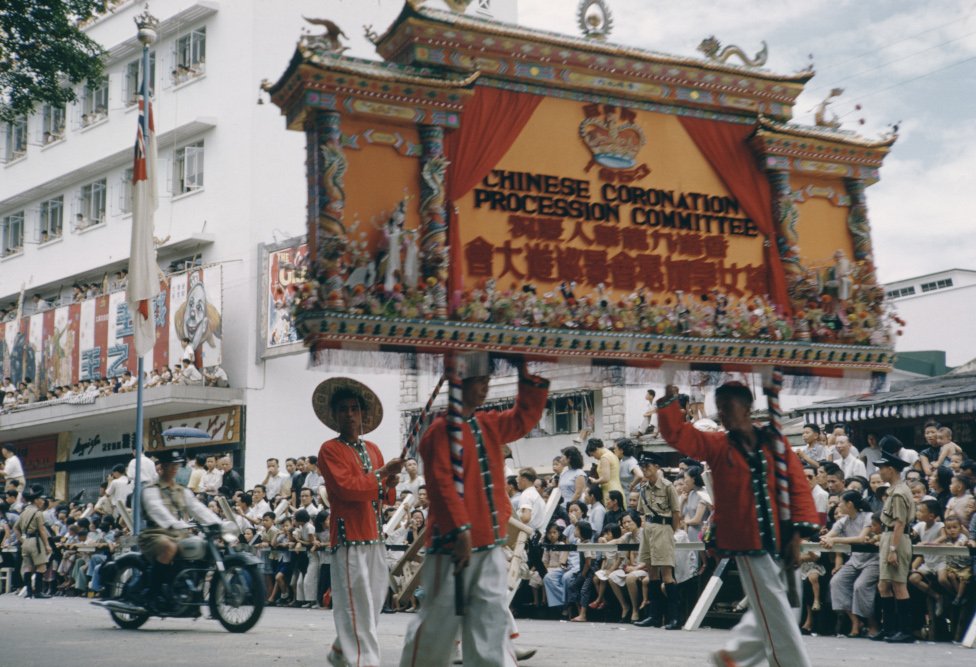 「香港九龍華人慶祝英女皇加冕會景巡遊大會」牌匾通過九龍旺角彌敦道東樂戲院（3/6/1953）