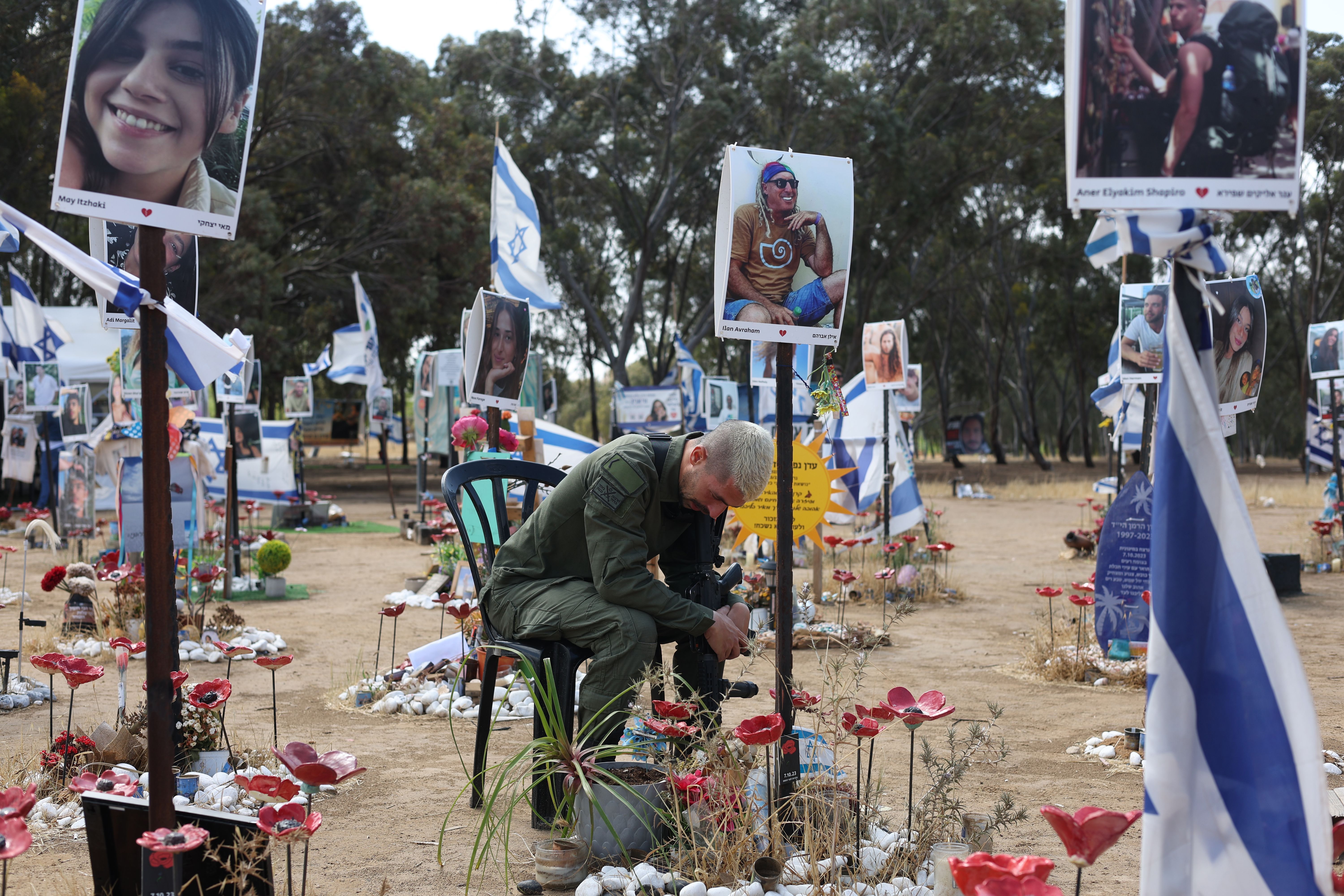 Izraelski vojnik sedi na stolicipognute glave među cvećem na mestu gde je Hamas ubio učesnike festivala