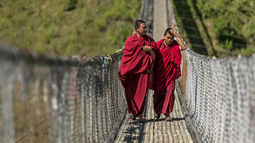 Dos monjes budistas caminando por un puente colgante