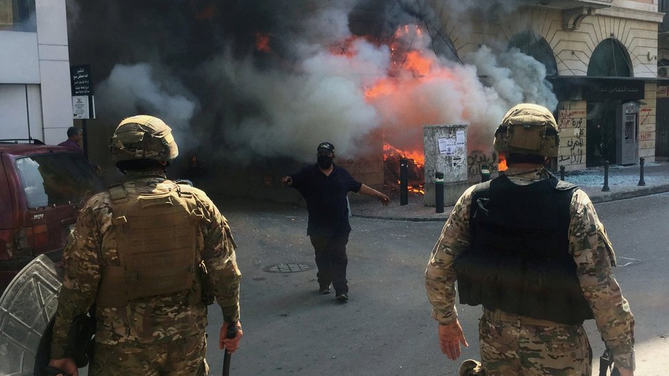 Мужчина показывает солдатам перед банком, подожженным протестующими в Триполи, Ливан (28 апреля 2020 г.)
