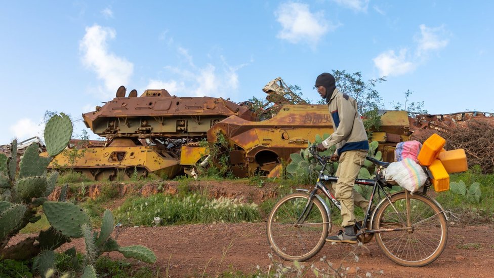 Eritrean man riding a bicycle in front of the military tank graveyard, Central region, Asmara, Eritrea on August 22, 2019 in Asmara, Eritrea.