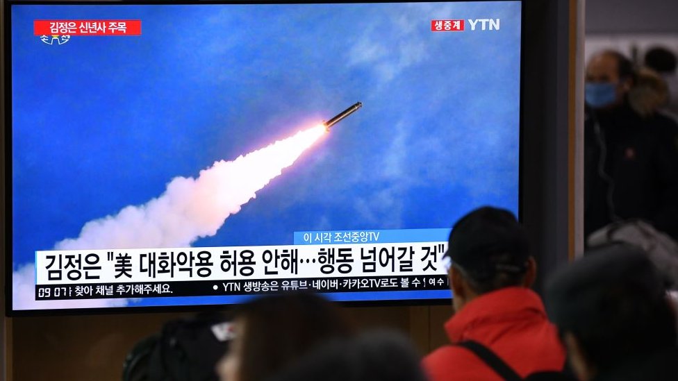 Люди смотрят телевизионную новостную программу, в которой демонстрируются архивные кадры испытаний ракеты Северной Кореей,