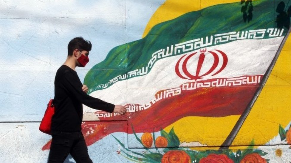 An Iranian boy walks past a mural with Iran's national flag