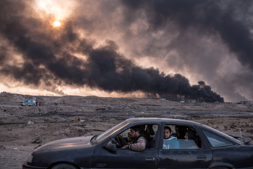 Семья бежит от боевых действий в Мосуле, втором по величине городе Ирака, когда 12 ноября 2016 года в Кайяре, Ирак, сгорели нефтяные месторождения.