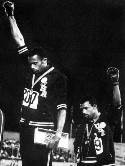 Los gestos de protesta durante el himno de EE.UU. no se limitan a la actualidad. Los atletas Tommie Smith y John Carlos levantaron sus puños durante la ceremonia de entrega de medallas de los Juegos Olímpicos de México 1968. Juegos Olímpicos de México 1968.