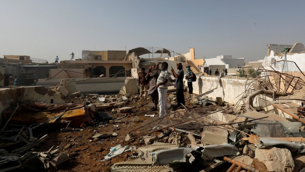 Locals are standing on the roof of a house where debris can be seen