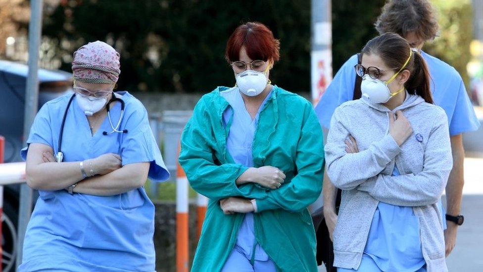People and health workers wear protective face masks outside the hospital in Padua, Veneto region