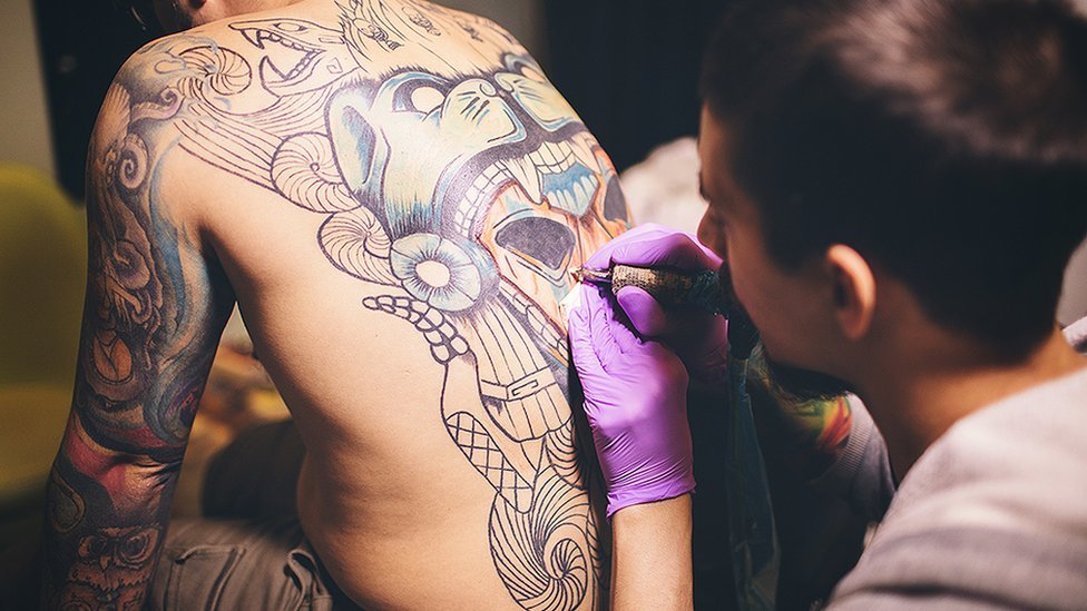 Un hombre dibujando un tatuaje en la espalda de otro.