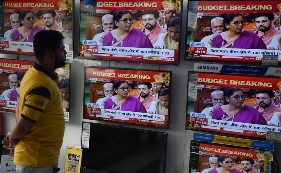 Индийский продавец наблюдает, как министр финансов Индии Нирмала Ситхараман выступает с речью о бюджете на телеэкранах в магазине электроники в Нью-Дели 5 июля 2019 г.
