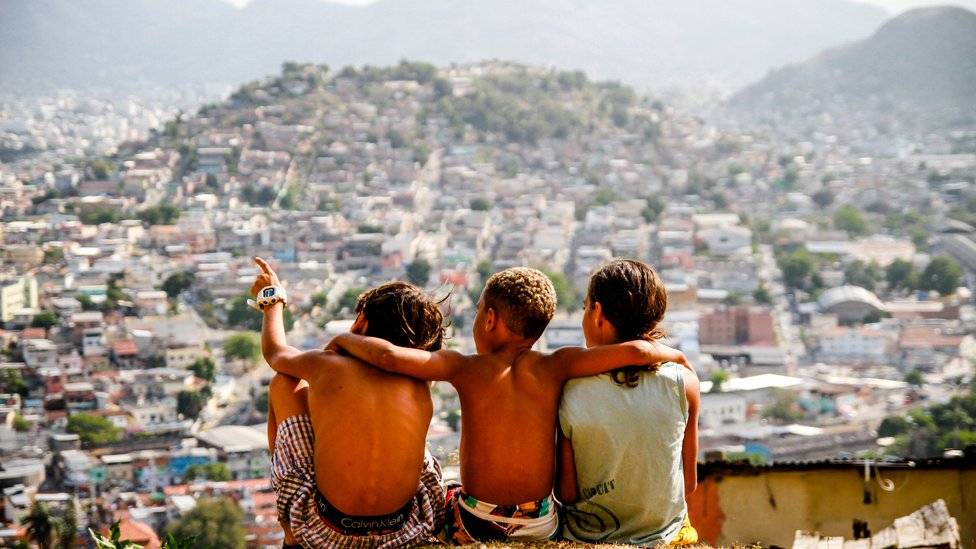 Tres niños en la cima de una favela contemplando la vista.