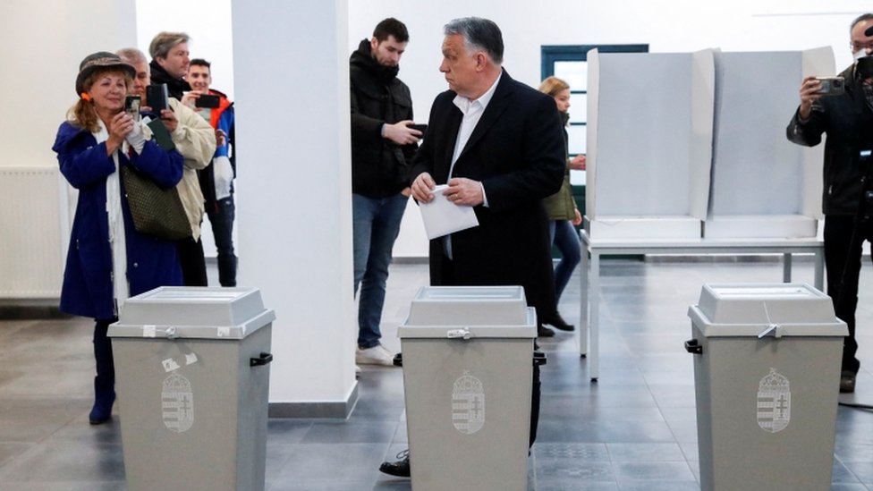 Orban sostiene una papeleta de votación frente a las urnas
