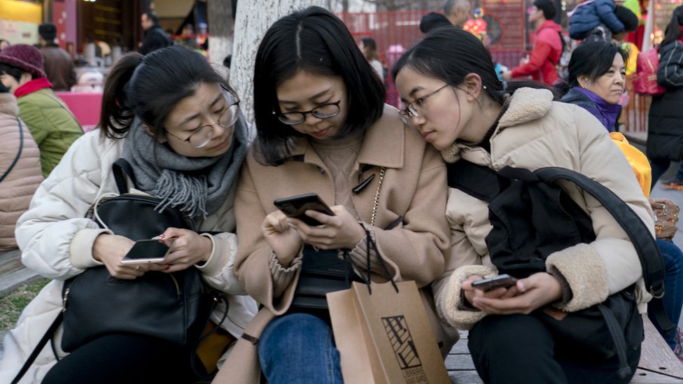 Mujeres mirando un teléfono en una silla en la calle.