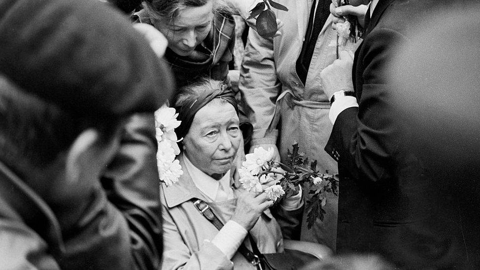 Beauvoir segura flores no funeral de Sartre, amparada por outras pessoas
