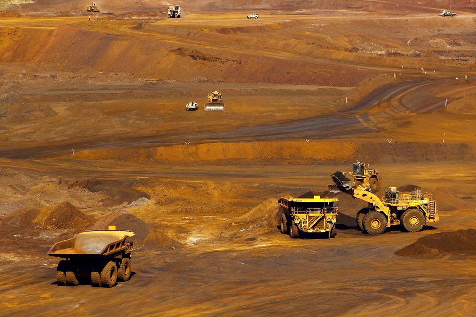 Рабочие стоят вокруг машины, когда грузовик загружается железной рудой в Fortescue Metals Group