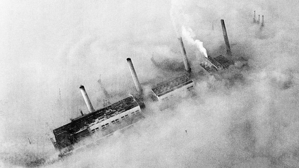 As chaminés de uma fábrica do East End em meio à fumaça da poluição que cobre Londres em 1952