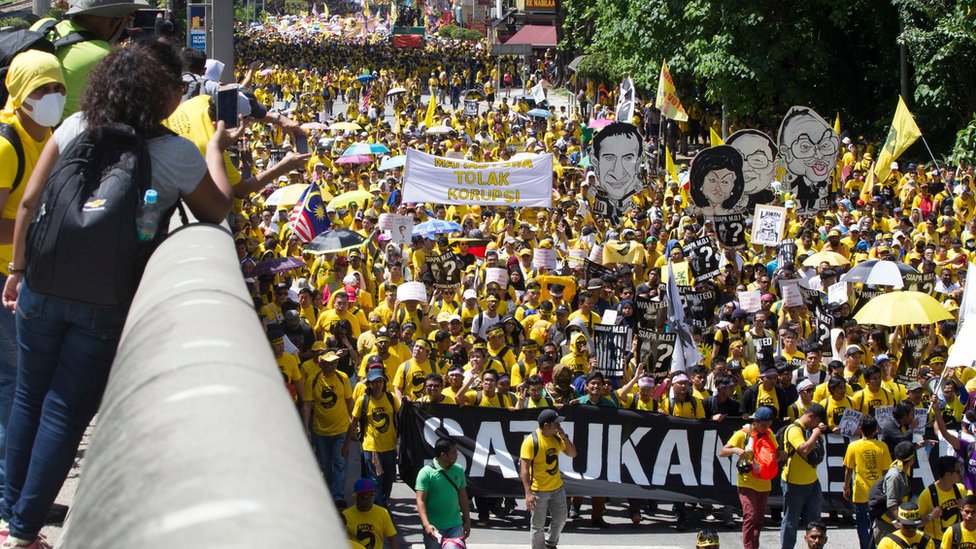 Протестующие в желтых рубашках в Куала-Лумпуре держат карикатуры