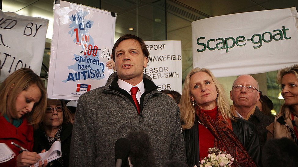 Andrew Wakefield standing with protesters next to a sign saying "Scape-goat" (sic)