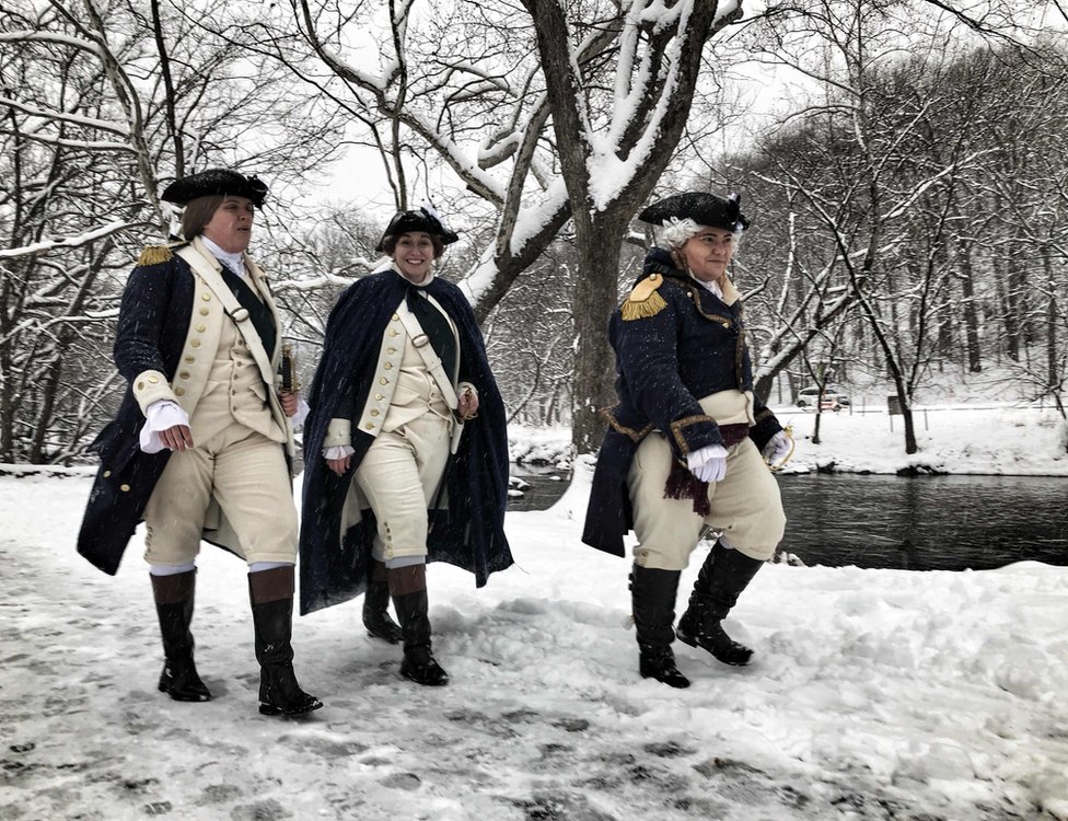 Three women wear American Revolution outfits while walking in snow
