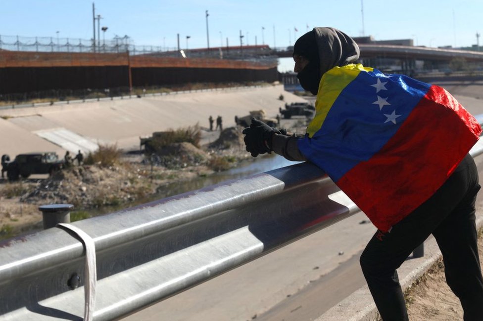Envuelto con la bandera de Venezuela, Alejandro Rojas, un migrante venezolano de 22 años, mira hacia Estados Unidos desde el otro lado de la valla fronteriza, en Ciudad Juárez, Chihuahua, México, el 20 de diciembre de 2022.