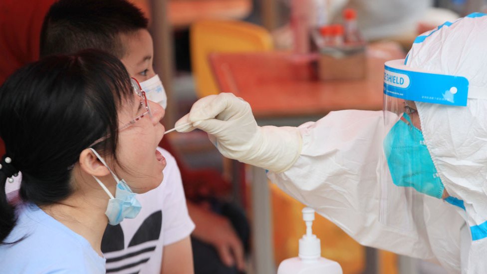 Funcionário coloca swab na boca de uma pessoa para fazer teste de covid-19 em Nanjing