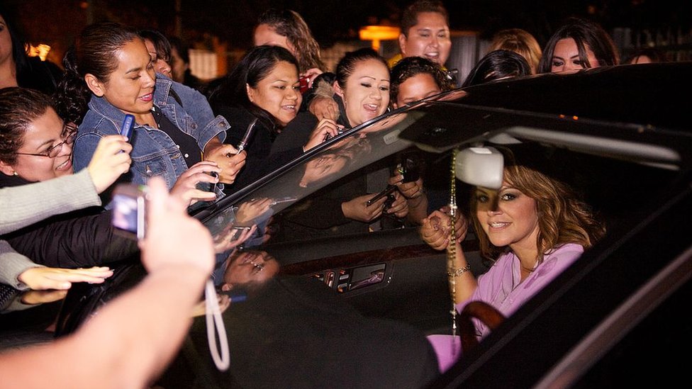 Jenni Rivera en un auto rodeada de fanáticos