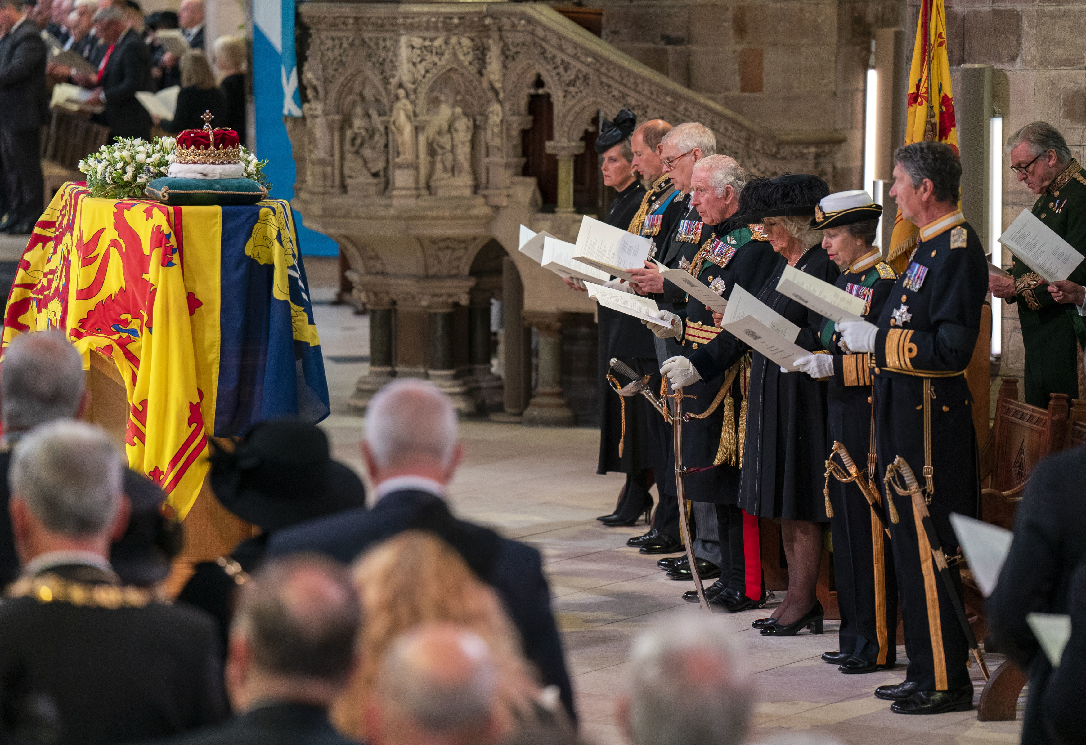 Membros da família real enfileirados, em pé, em frente a caixão