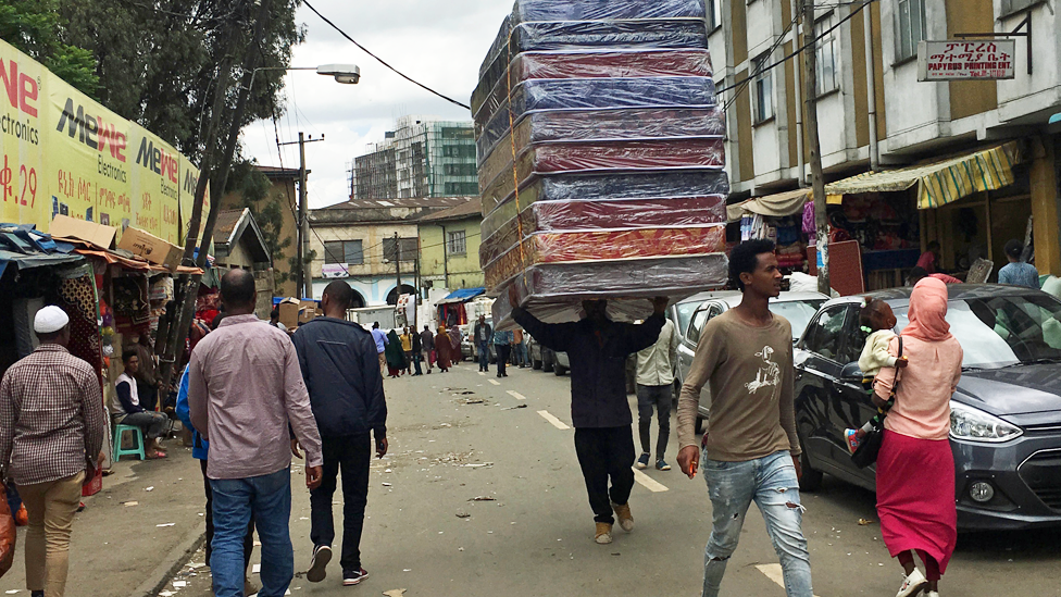 Мужчина с матрасами на голове по улице в районе Боле-Микаэль в Аддис-Абебе в Эфиопии
