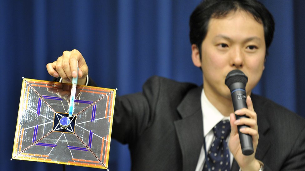 El científico Yuichi Tsuda sosteniendo un modelo del satélite IKAROS en una conferencia.