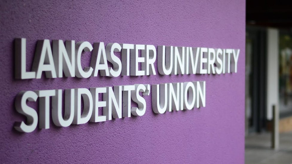 Белый логотип Союза студентов Ланкастерского университета на фиолетовой стене
