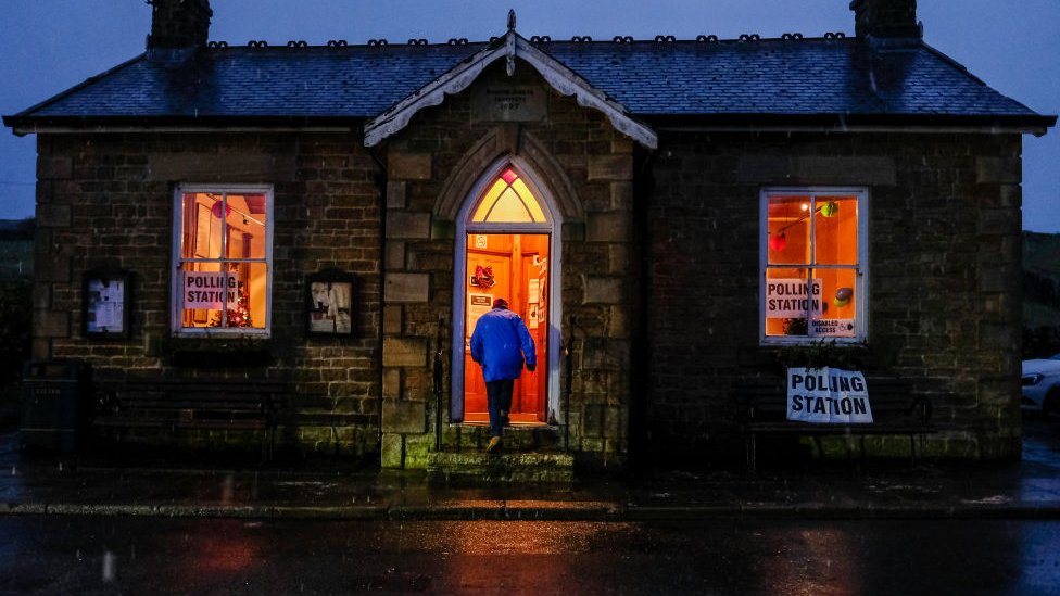 Мужчина входит на избирательный участок, когда на Северных Пеннинах падает снег