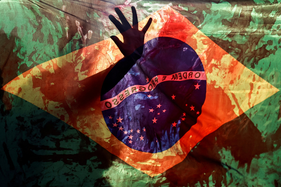 السكان الأصليون يرفعون علم البرازيل وهو ملطخ بالدم، خلال مسيرة احتجاجية ضد إقرار مجلس النواب مشروع قانون يحد من ترسيم أراضي السكان الأصليين، برازيليا، البرازيل، 30 مايو 2023.