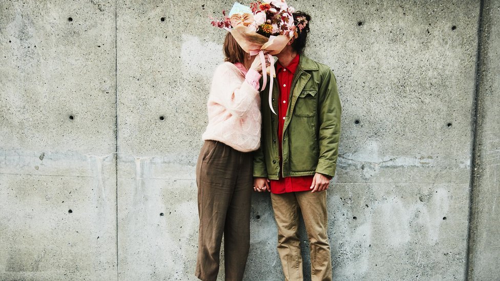 A couple kiss behind a bunch of flowers