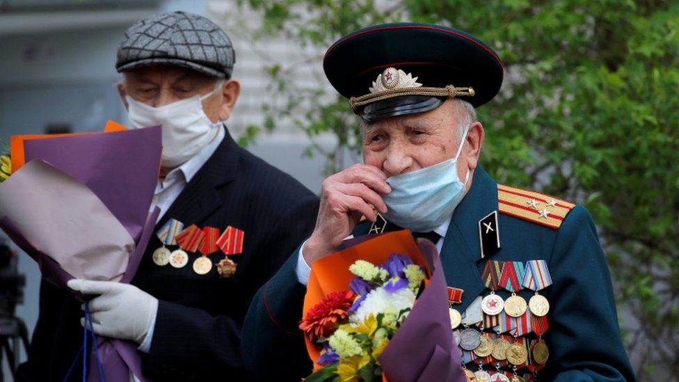 Belarusian veterans Pyotr Vorobyov and Pavel Eroshenko cover their faces with protective masks as they listen to a military band