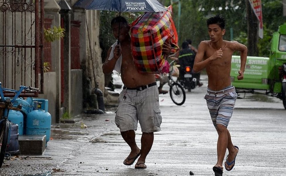 A resident carries his belongings to a safer place while another runs as rains started to pour, with Typhoon Mangkhut approaching the city of Tuguegarao, Cagayan province, north of Manila on September 14, 2018.