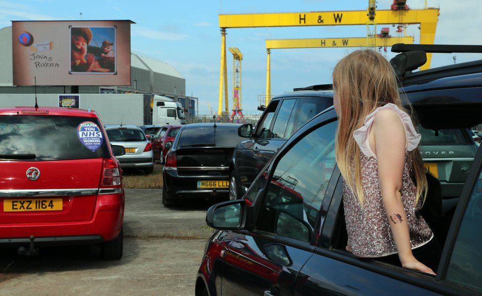 Девушка высовывается из машины, чтобы посмотреть на экран в кинотеатре для автомобилей