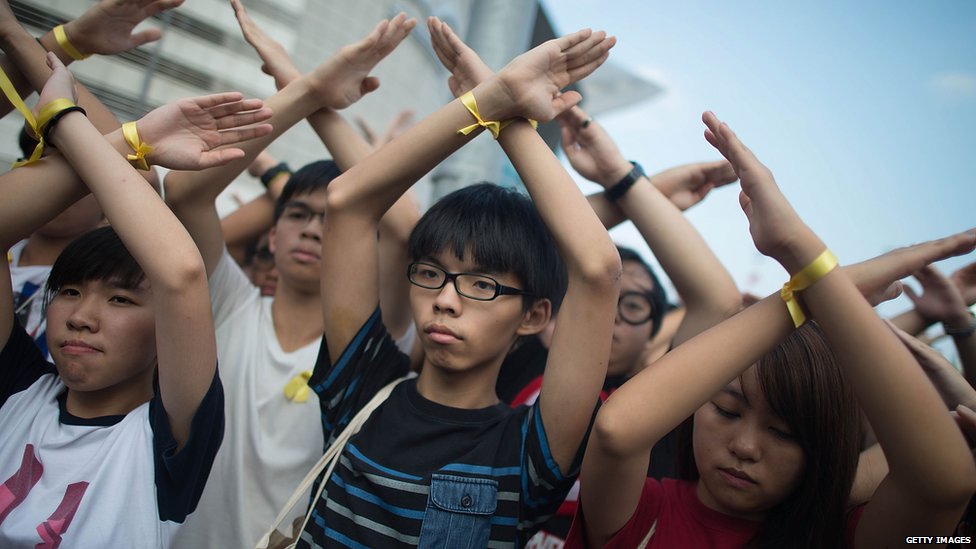 Студенческая продемократическая группа Организатор Scholarism Джошуа Вонг (C) делает жест на церемонии поднятия флага на площади Золотой Баухинии 1 октября 2014 года в Гонконге.