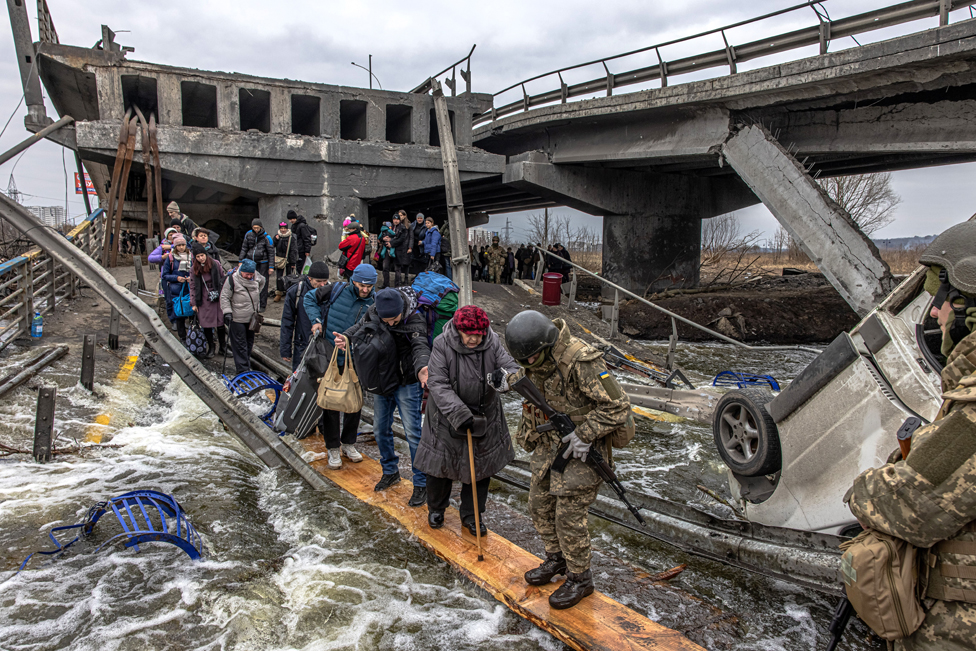 People cross the river via a makeshift bridge as they flee the frontline town of Irpin, near Kyiv, Ukraine - 7 March 2022.
