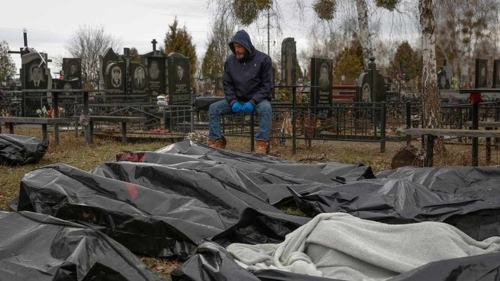Radnik pogrebnog preduzeća sedi pored tela civila u Buči
