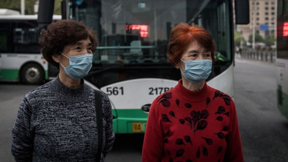 Dos mujeres en Wuhan esperan abordar un autobús después de la reanudación del servicio.