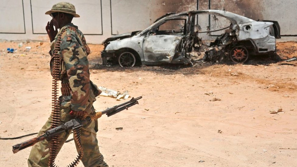 A Somali soldier patrols next to the burnt-out wreckage of a car that was used by suspected al-shabab fighters on April 16, 2017.