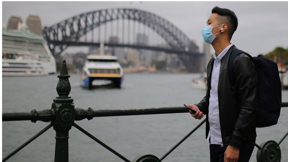 Мужчина в маске перед мостом Харбор-Бридж в Сиднее, Австралия.