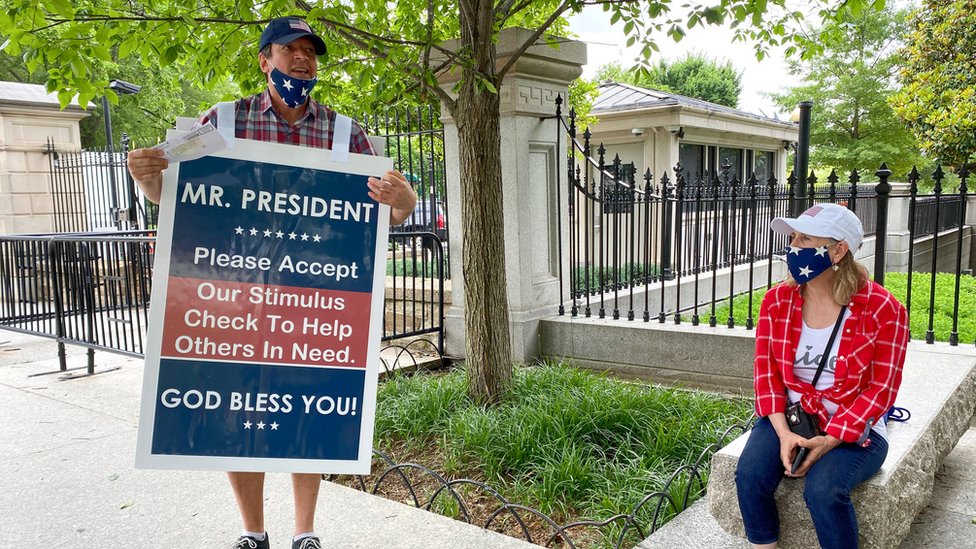 Un hombre con un cartel en el que ofrece su cheque al presidente Trump para que se lo dé a alguien más necesitado