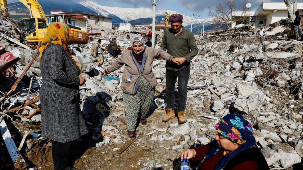 امرأة تتلقى المساعدة أثناء سيرها وسط الأنقاض والأضرار بعد الزلزال الذي ضرب مدينة غازي عنتاب بتركيا
