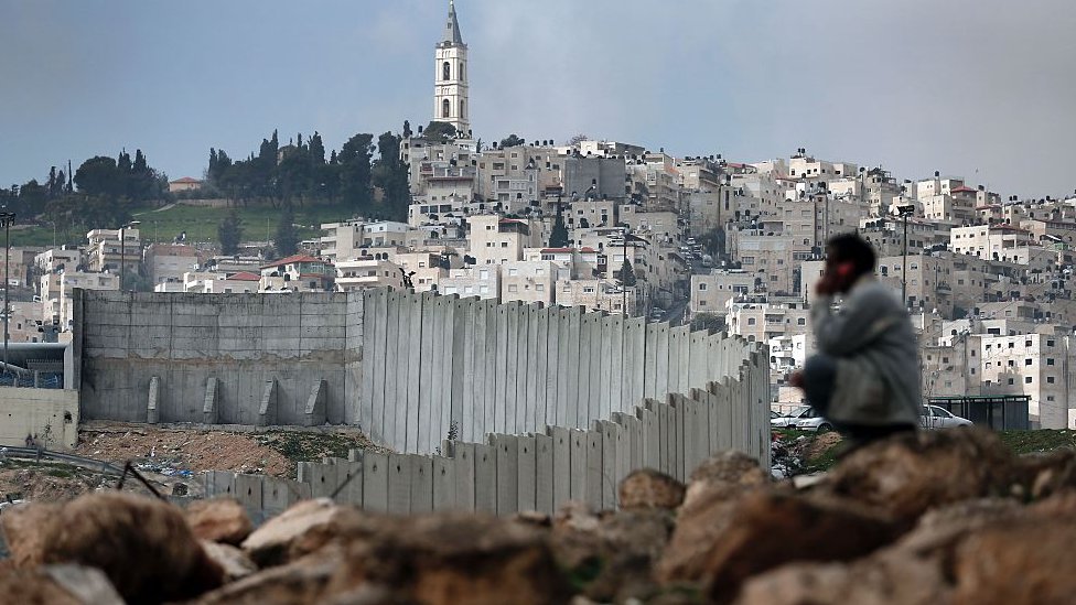 Hombre palestino sentado cerca de la controvertida barrera de separación de Israel en Jerusalén.